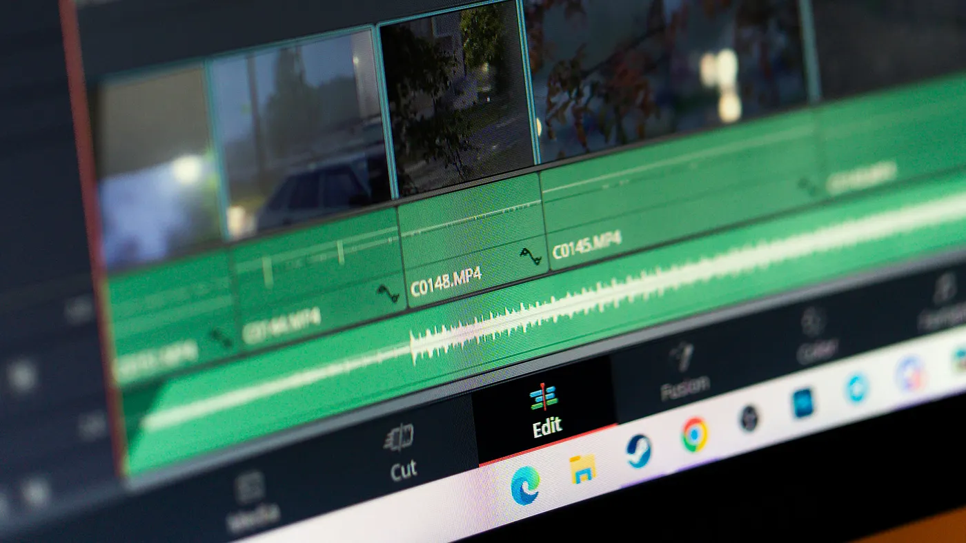 Close-up of a computer screen showing a DaVinci Resolve editing timeline with multiple video clips and a green audio waveform in a professional editing software interface.