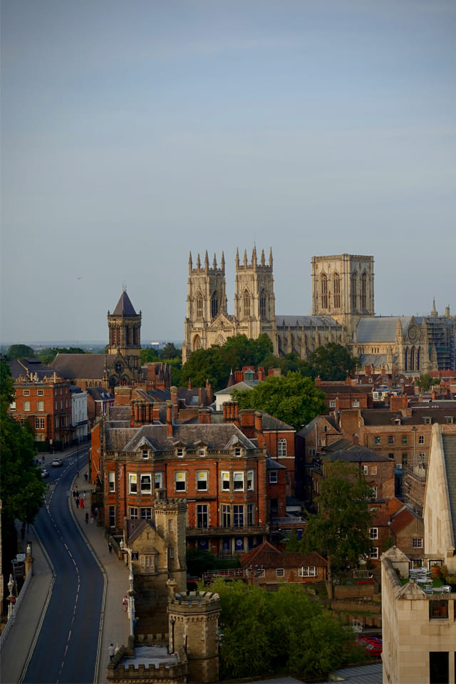 Elevated view of York’s historic cityscape with red-brick buildings, tree-lined streets, and the large Gothic cathedral dominating the skyline.
